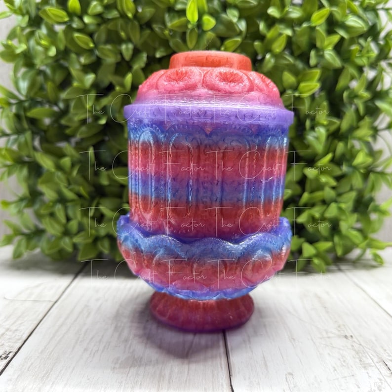 May include: A colorful, decorative resin candle holder. The holder features a layered design with shades of red, purple, and blue. The base is a deep red, transitioning to blue and purple in the middle, and topped with red. The Craft Factor is printed on the side.