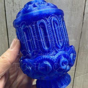 May include: A vibrant blue decorative object with intricate, ornate detailing. The object has a rounded top and base, with vertical arched patterns and floral-like embellishments. The Craft Factor text is visible on the object.