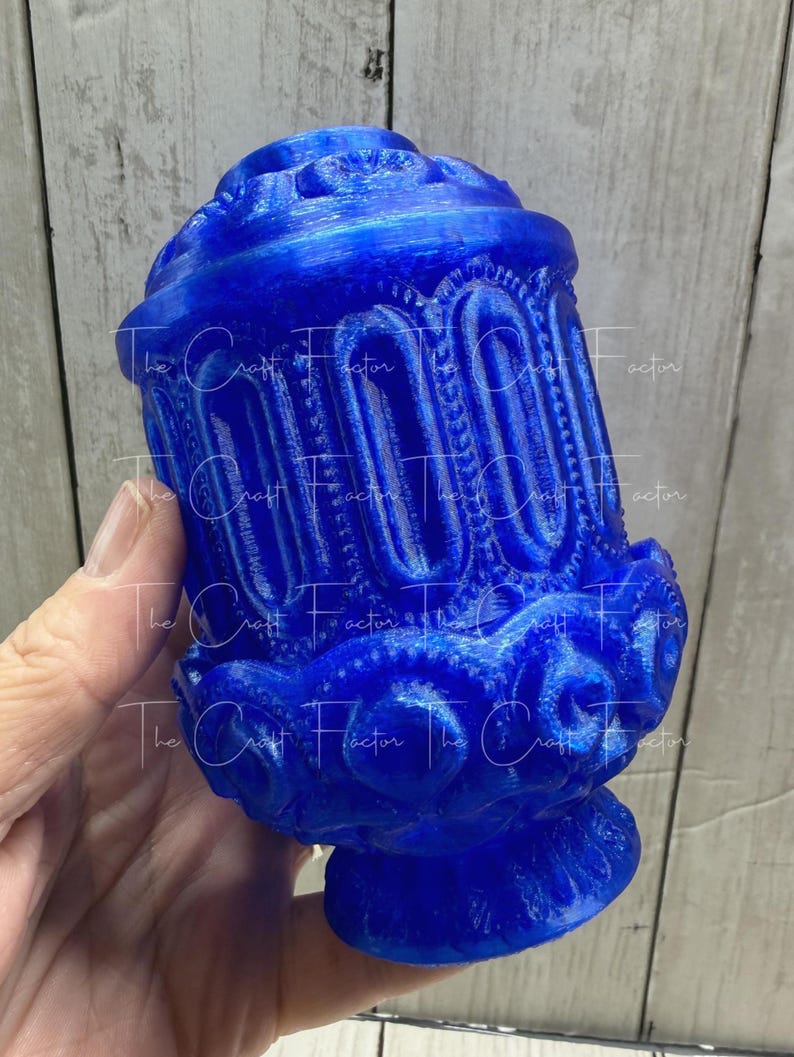 May include: A vibrant blue decorative object with intricate, ornate detailing. The object has a rounded top and base, with vertical arched patterns and floral-like embellishments. The Craft Factor text is visible on the object.