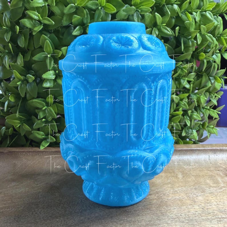 May include: A light blue decorative jar with ornate detailing. The jar has a rounded base and a flared top, with a series of vertical columns and floral-like patterns. The text "The Craft Factor" is watermarked on the jar.