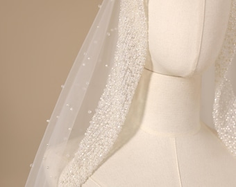 May include: A white bridal veil featuring a dense border of small, shimmering beads along the edge that frames the face. The sheer tulle fabric is scattered with individual, spaced-out pearls throughout the length of the veil, creating a delicate texture.