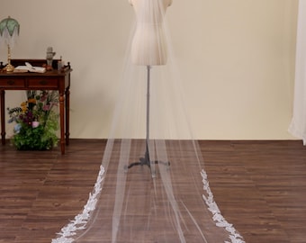 May include: A long, floor-length white bridal veil made of sheer tulle fabric. The veil features intricate white floral lace embroidery along the curved bottom edge and sides, creating a decorative border that pools on the floor.