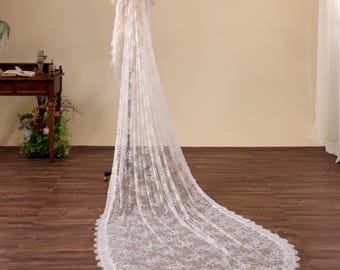 May include: A long, white lace wedding veil displayed on a mannequin. The veil is intricately detailed with floral patterns and a scalloped edge. The veil is draped to show its full length and design, perfect for bridal wear.