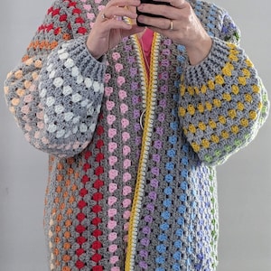 May include: A colourful crochet cardigan with a granny square pattern in shades of grey, pink, yellow, orange, red, blue, and green. The cardigan has a yellow trim and a long, open front.