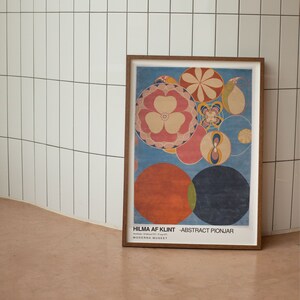 May include: A framed poster featuring a colourful abstract design with circles and flowers. The poster is titled "HILMA AF KLINT - ABSTRACT PIONJAR" and includes the text "Moderna Museet".