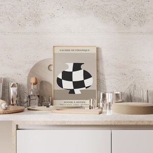 May include: A framed poster with a black and white checkered vase on a beige background. The poster is titled "Galerie de C&eacute;ramique" and "Poterie &agrave; Motifs".