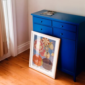 May include: A blue dresser with four drawers and a framed print of a colourful abstract design. The print is titled "Hilma af Klint - Abstract Pionjar".