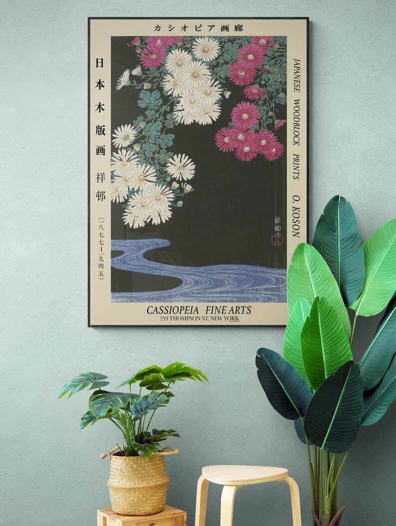 May include: A vintage Japanese woodblock print of white and pink chrysanthemums with a blue stream flowing through the bottom. The print is framed and has the text "JAPANESE WOODBLOCK PRINTS O. KOSON" and "CASSIOPEIA FINE ARTS 219 THOMPSON ST. NEW YORK" printed on it.