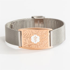 May include: A silver mesh bracelet with a rose gold medical alert tag. The tag has a white medical symbol and a floral design.