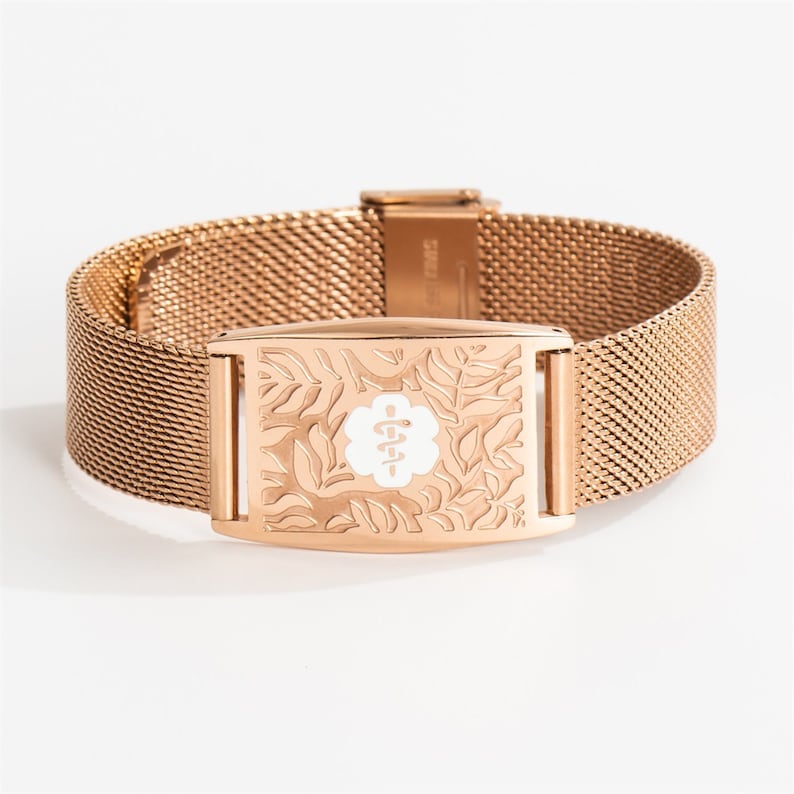 May include: A rose gold medical alert bracelet with a mesh band and a rectangular engraved plate featuring a floral design and a medical symbol.