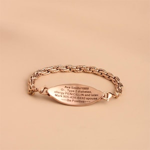 May include: A rose gold-toned medical alert bracelet featuring a textured rope-style chain and an oval-shaped identification plate. The plate is engraved with the text: Ava Smith/1988, O-, Type 2 diabetes, allergy PENICILLIN and latex, Mark 905-43X-64X0 spouse, ---Be Positive---.
