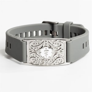 May include: Grey silicone bracelet with a silver medical alert tag. The tag has an engraved design and the word "MED" in white.
