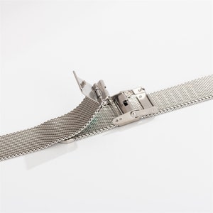 May include: A silver metal watch band with a clasp closure. The band is made of a fine mesh material.