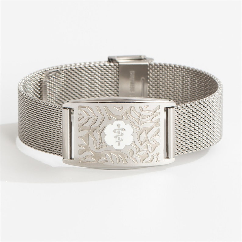 May include: A silver medical alert bracelet with a mesh band and a rectangular tag featuring a white medical symbol and a floral design.
