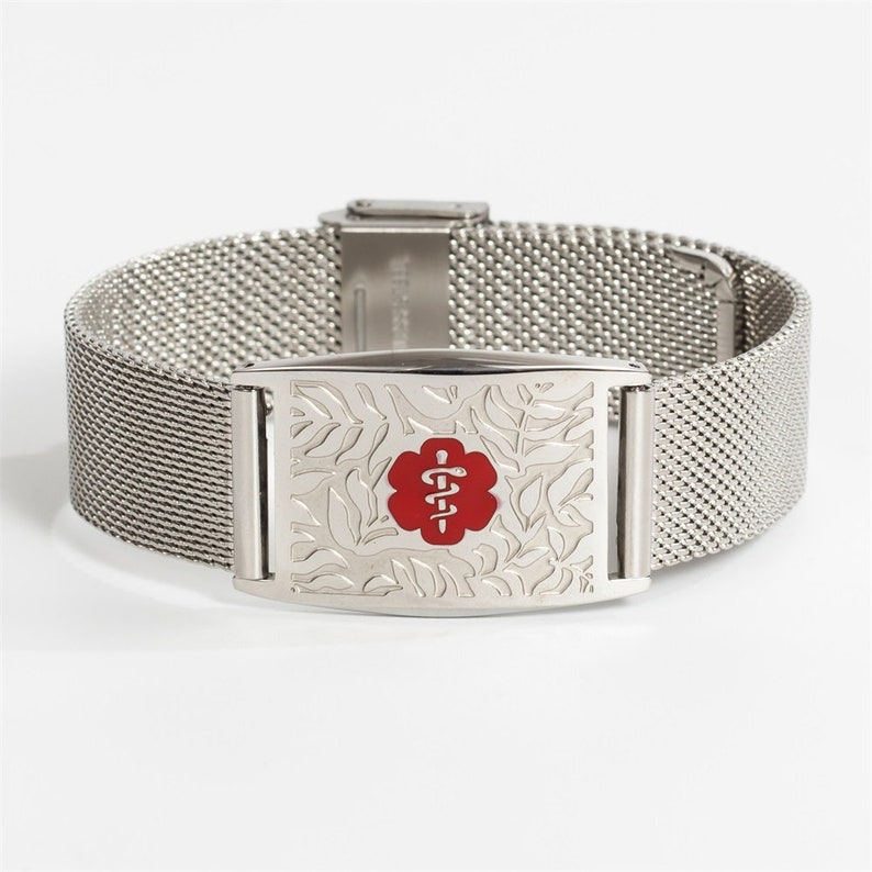 May include: A silver medical alert bracelet with a mesh band and a rectangular tag. The tag has a floral design and a red medical symbol with a snake and staff.