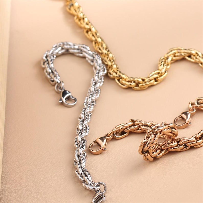 May include: Three metal chain bracelets in silver, gold, and rose gold tones. Each bracelet features a thick, braided rope-style link design and is finished with a secure lobster claw clasp, providing a consistent look across all three pieces.