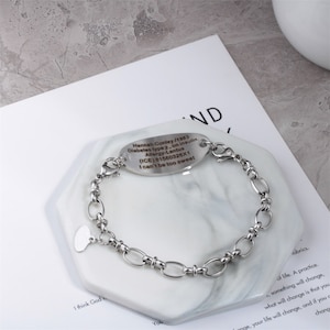 May include: A silver bracelet with a heart charm and an oval tag engraved with medical information. The tag reads "Hannah Conley / 1983 Diabetes type 2. on insulin. Allergy-Lantus (ICE) 81560326&times;1 I can't be too sweet"