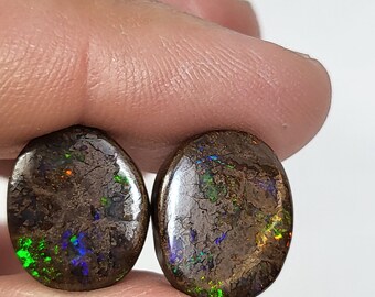 May include: Two oval-shaped opal gemstones with a dark brown base and iridescent green, blue, and red flashes.