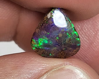 May include: A teardrop-shaped opal gemstone with a dark brown base and iridescent green, purple, and blue flashes.