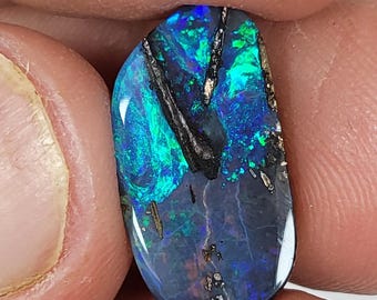 May include: A dark blue, green, and black opal gemstone with a rough, natural shape. The opal has a high shine and a variety of colors.