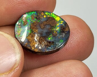 May include: A round, oval-shaped opal gemstone with a dark brown base and a colorful iridescent surface. The opal has a mix of green, blue, yellow, and orange colors.