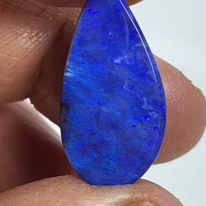 May include: A teardrop-shaped polished gemstone featuring a vibrant, deep blue color with subtle, swirling iridescent patterns throughout its surface. The stone has a smooth, reflective finish and displays varying shades of blue and hints of violet.