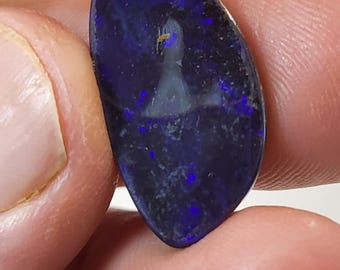 May include: A dark blue, oval-shaped opal gemstone with a white, cloudy pattern inside. The opal is held in a hand.