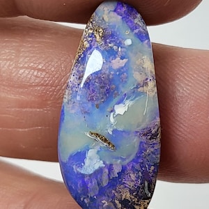 May include: A teardrop-shaped opal cabochon with a blue, purple, and white pattern. The opal has a gold and black matrix.