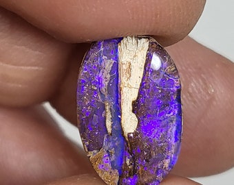 May include: A purple and brown opal gemstone with a white vein running through it. The opal is oval shaped and has a high polish.