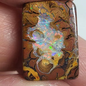 May include: A rectangular boulder opal gemstone featuring a dark brown ironstone matrix with intricate, branching patterns. The center displays a vibrant, multi-colored play-of-color with flashes of bright red, green, blue, and yellow light.