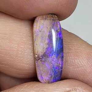 May include: A purple and brown oval-shaped opal gemstone with a white flash of light.