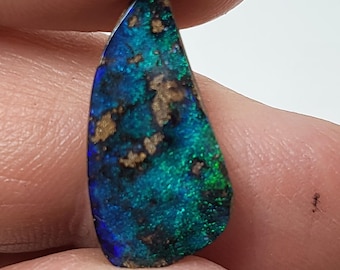 May include: A teardrop-shaped opal gemstone with a dark blue and green iridescent sheen. The opal has a black base with brown inclusions.