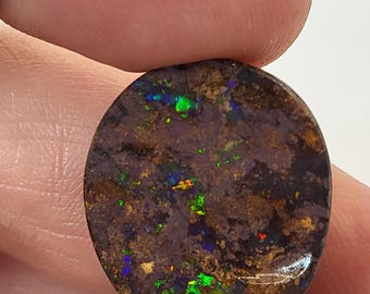 May include: A round, dark brown opal with green, blue, and red flashes of color. The opal is set in a silver ring.