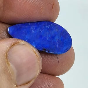 May include: A polished, teardrop-shaped gemstone featuring a vibrant, deep blue color with subtle, lighter blue and white internal patterns and a smooth, reflective surface. The stone displays a rich, saturated hue throughout its entire form.