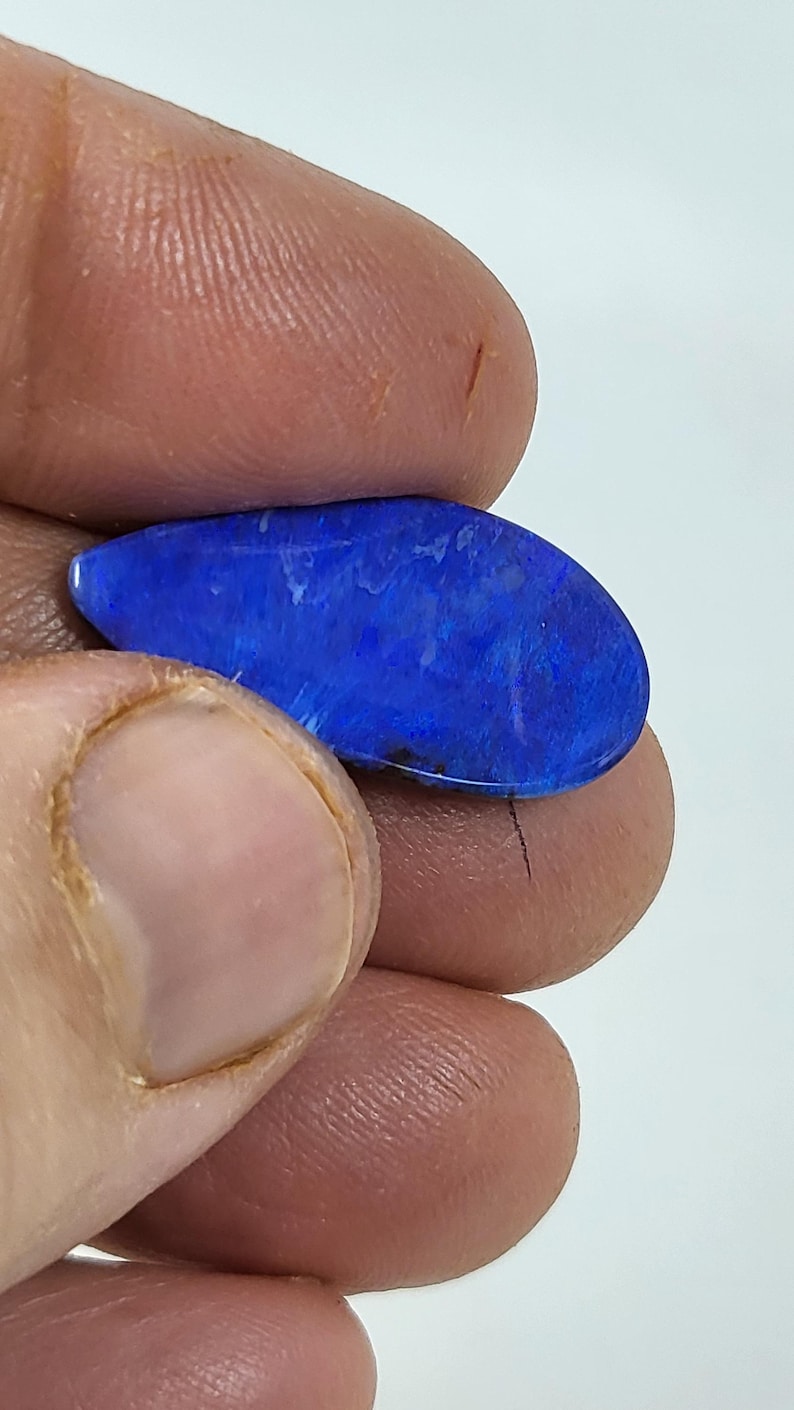 May include: A polished, teardrop-shaped gemstone featuring a vibrant, deep blue color with subtle, lighter blue and white internal patterns and a smooth, reflective surface. The stone displays a rich, saturated hue throughout its entire form.