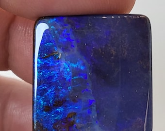 May include: A square-shaped blue opal gemstone with a dark blue and purple iridescent sheen.