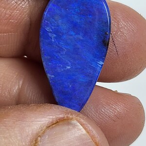May include: A teardrop-shaped gemstone featuring a vibrant, deep blue color with iridescent flashes and subtle light blue streaks throughout its polished surface. The stone displays a smooth, rounded finish and a distinct play of color.