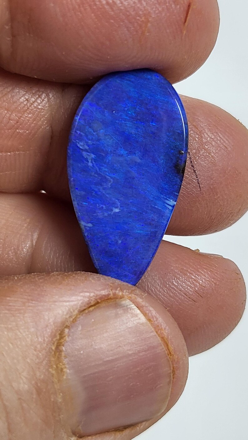 May include: A teardrop-shaped gemstone featuring a vibrant, deep blue color with iridescent flashes and subtle light blue streaks throughout its polished surface. The stone displays a smooth, rounded finish and a distinct play of color.