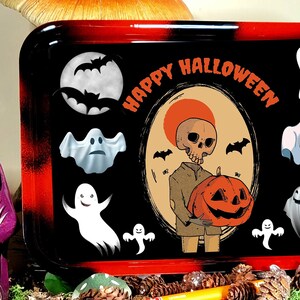 May include: A rectangular rolling tray with a black and red gradient border. The centre features a graphic of a skeleton holding a pumpkin, surrounded by ghosts, bats, a full moon, and the orange text "HAPPY HALLOWEEN" printed on a black background.