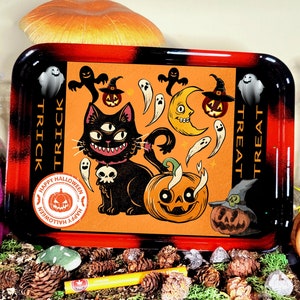 May include: A rectangular rolling tray with a black and red gradient border and an orange centre featuring a black cat with three eyes, a skull pendant, pumpkins, ghosts, and a crescent moon. The text reads TRICK TRICK and TREAT TREAT.