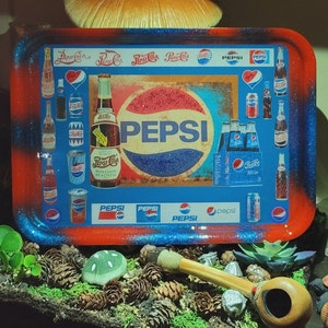 May include: A rectangular rolling tray with a red and blue glitter border featuring a collage of vintage Pepsi-Cola logos, glass bottles, and soda cans. The central design displays the Pepsi logo with the text Pepsi-Cola Refreshing Healthful.