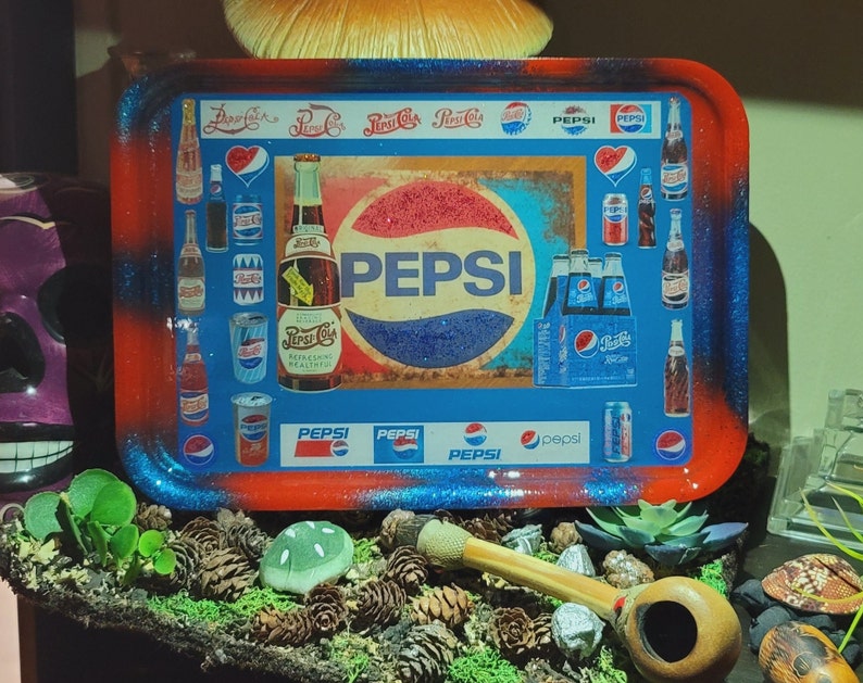 May include: A rectangular rolling tray with a red and blue glitter border featuring a collage of vintage Pepsi-Cola logos, glass bottles, and soda cans. The central design displays the Pepsi logo with the text Pepsi-Cola Refreshing Healthful.