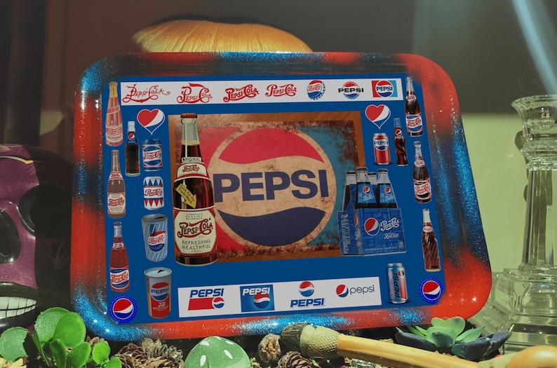 May include: A rectangular rolling tray with a red and blue glitter border featuring a collage of vintage Pepsi-Cola logos, glass bottles, and soda cans. The centre displays a large circular Pepsi logo with the text PEPSI in bold blue letters.
