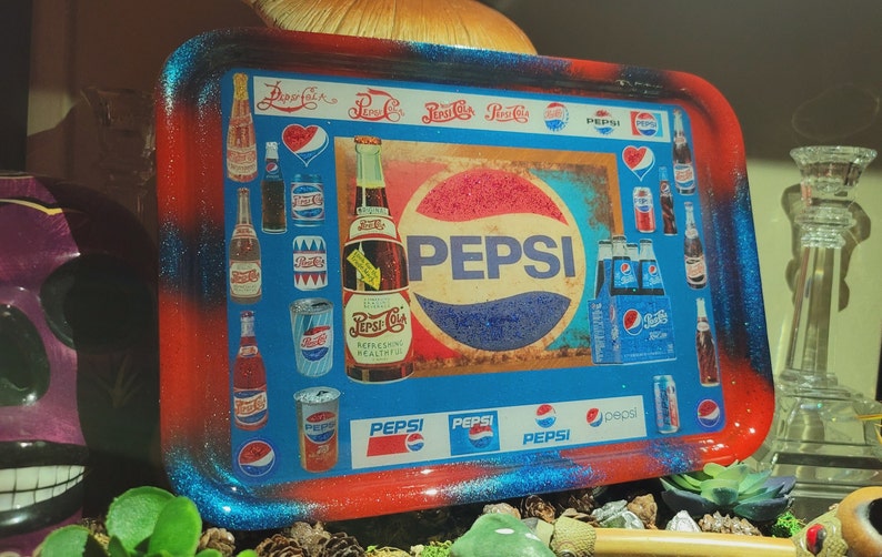 May include: A rectangular rolling tray with a glossy finish, featuring a red and blue gradient border. The centre displays various vintage Pepsi-Cola logos, imagery of glass bottles, aluminium cans, and a six-pack carton, all centred around the Pepsi logo.