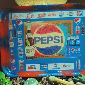 May include: A rectangular rolling tray featuring a collage of vintage Pepsi branding, including various soda bottles, cans, and the classic Pepsi logo. The tray has a glossy finish with a red and blue gradient border and rounded corners.