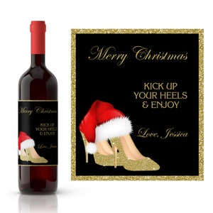 May include: A wine bottle label with a gold glitter background and a pair of gold glitter high heels with a red and white Santa hat. The text on the label reads "Merry Christmas Kick Up Your Heels & Enjoy Love, Jessica".