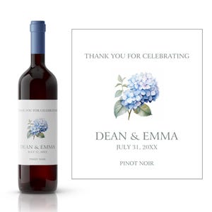 Könnte beinhalten: Ein Wein-Flaschenetikett für ein Hochzeitsgeschenk mit einer blauen Hortensien-Illustration. Das Etikett lautet "Vielen Dank fürs Feiern Dean & Emma 31. Juli 20XX Pinot Noir".