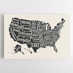 May include: A canvas print featuring a black and white map of the United States, with each state's name displayed in a bold, stylized font. The map is set against a cream-colored background.