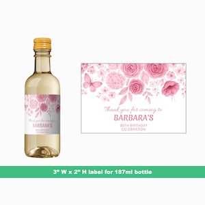 May include: A clear glass wine bottle with a gold cap and a label featuring pink floral designs. The label reads "Thank you for coming to BARBARA'S 90TH BIRTHDAY CELEBRATION." A matching card is displayed next to the bottle.