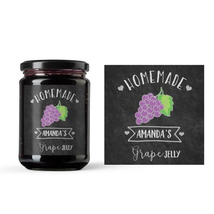 Puede incluir: Una etiqueta de pizarra negra y blanca con el texto "Homemade" y "Amanda's Grape Jelly" en texto blanco. Un racimo de uvas moradas con hojas verdes está ilustrado en la etiqueta.